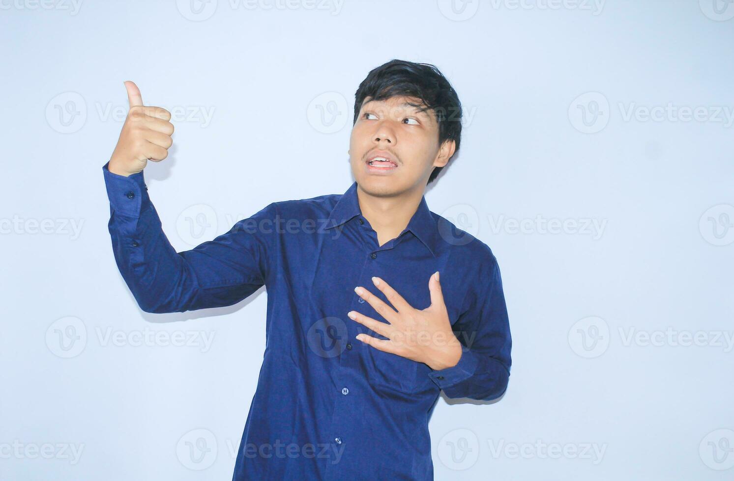 proud young asian man smiling with grateful face for survived from heart attack and has recovery is holding chest with thunbs up wearing navy shirt photo