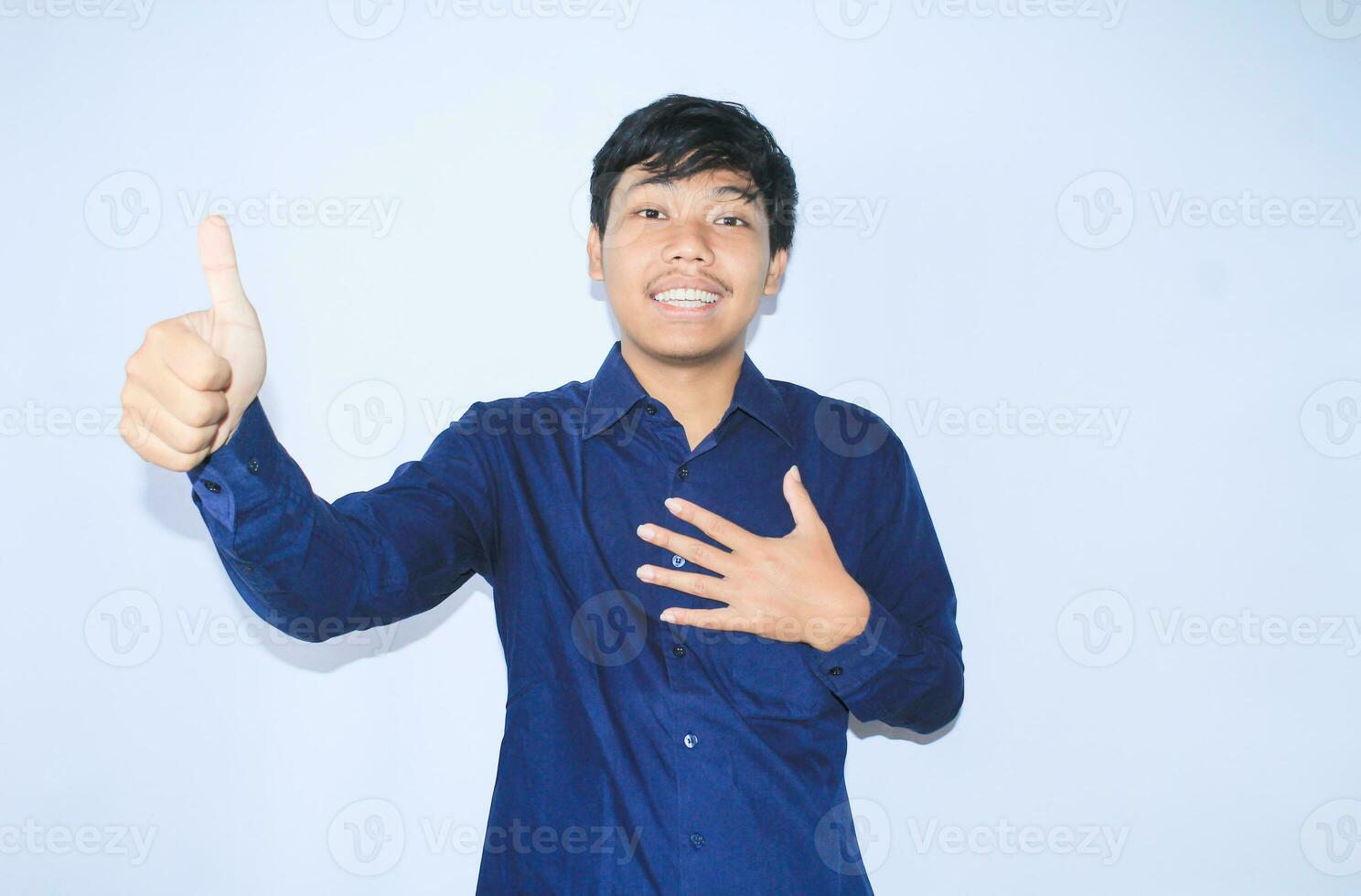 proud young asian man smiling with grateful face for survived from heart attack and has recovery is holding chest with thunbs up wearing navy shirt photo