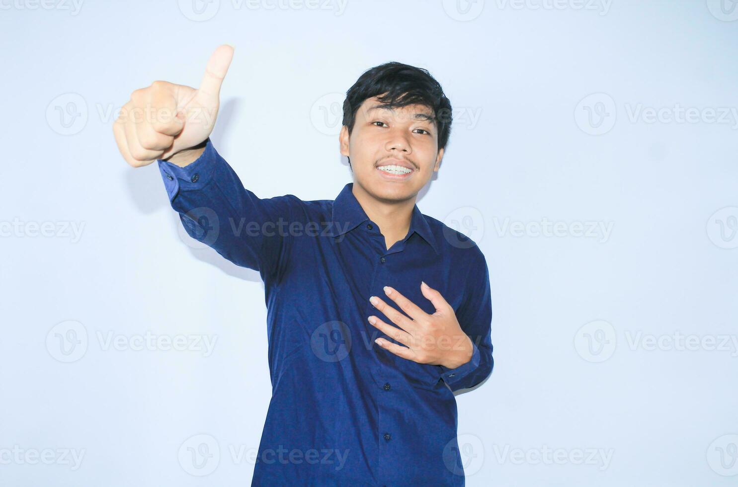 orgulloso joven asiático hombre sonriente con agradecido cara para sobrevivió desde corazón ataque y tiene recuperación es participación cofre con thunbs arriba vistiendo Armada camisa foto