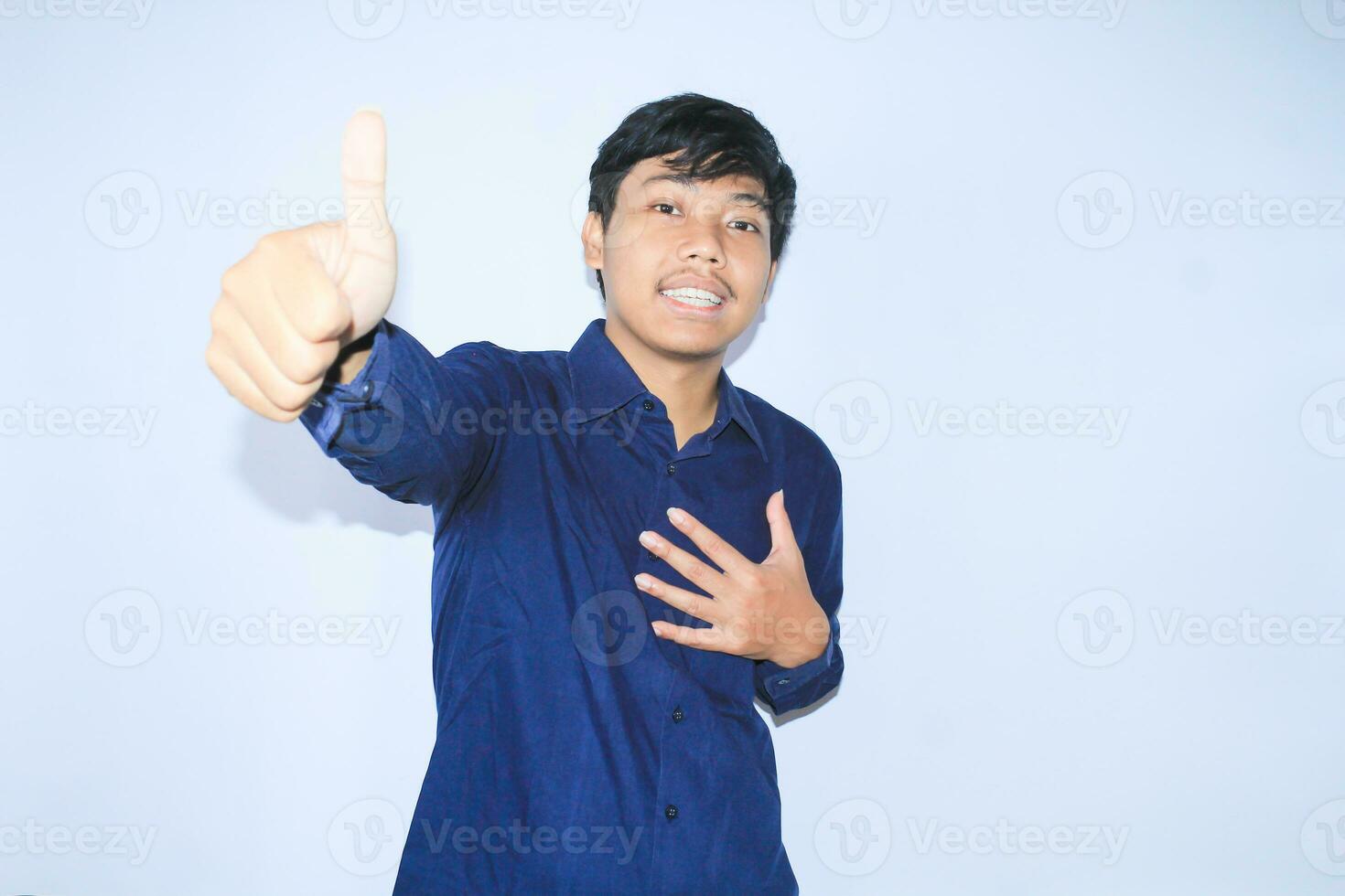 proud young asian man smiling with grateful face for survived from heart attack and has recovery is holding chest with thunbs up wearing navy shirt photo