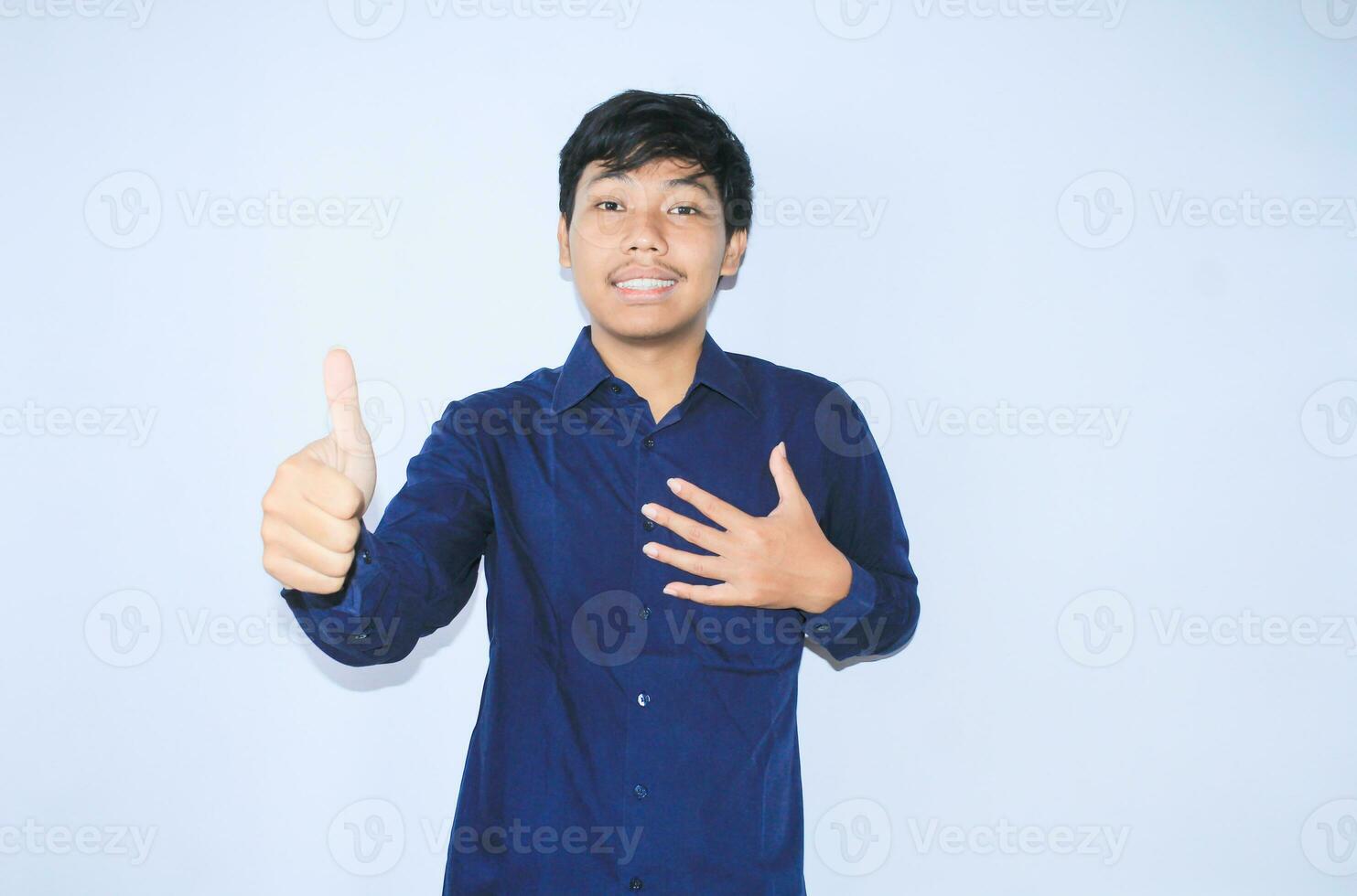 proud young asian man smiling with grateful face for survived from heart attack and has recovery is holding chest with thunbs up wearing navy shirt photo