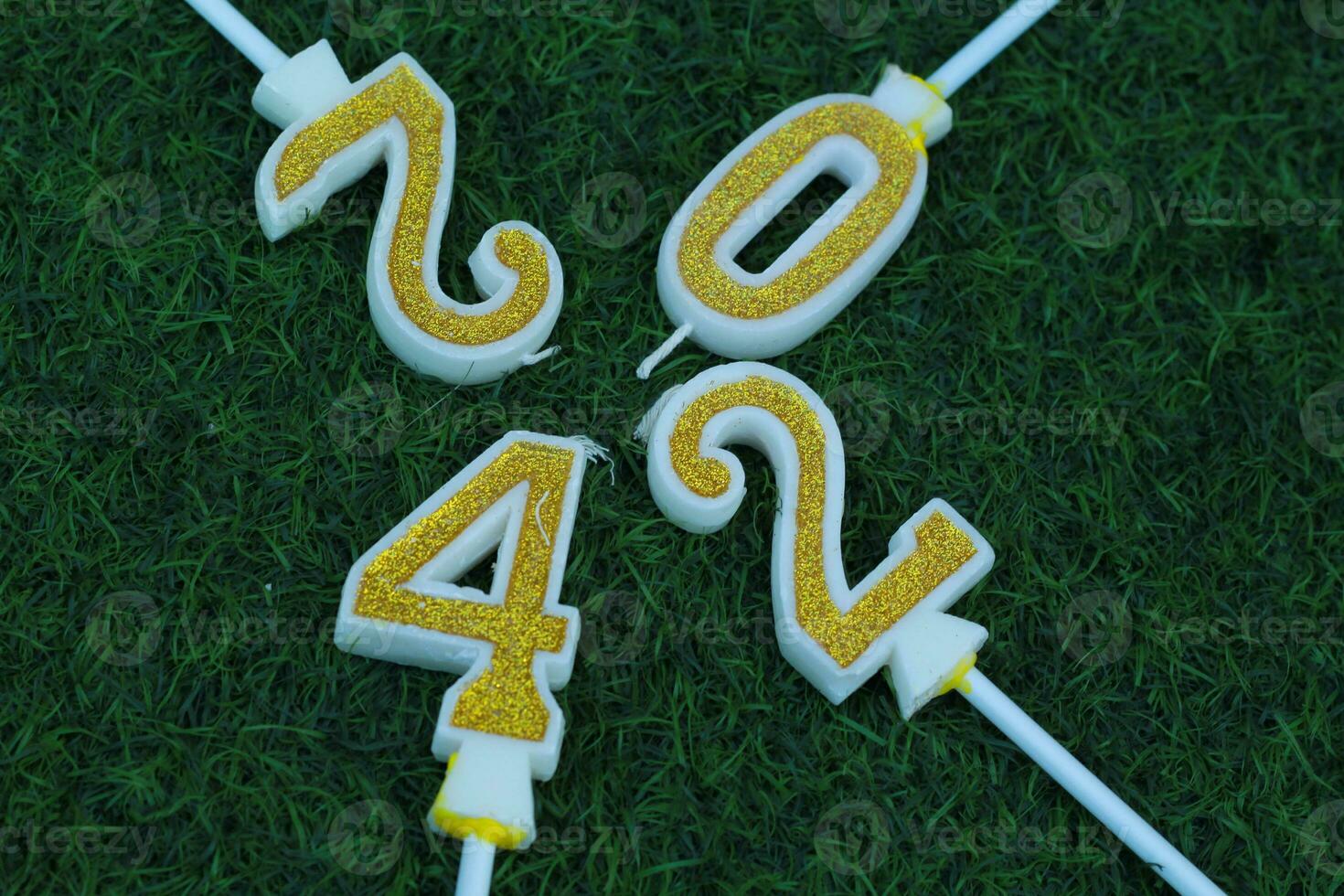 top view of glittering gold candle number 2024 above meadow with green grass, new year eve background concept photo