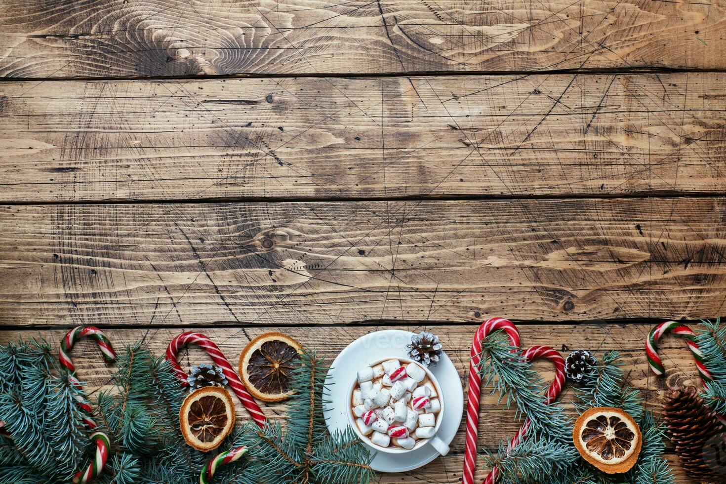 A Cup of hot chocolate with marshmallows. Christmas tree and decorations, cane caramel and oranges nuts Wooden background copy space. photo