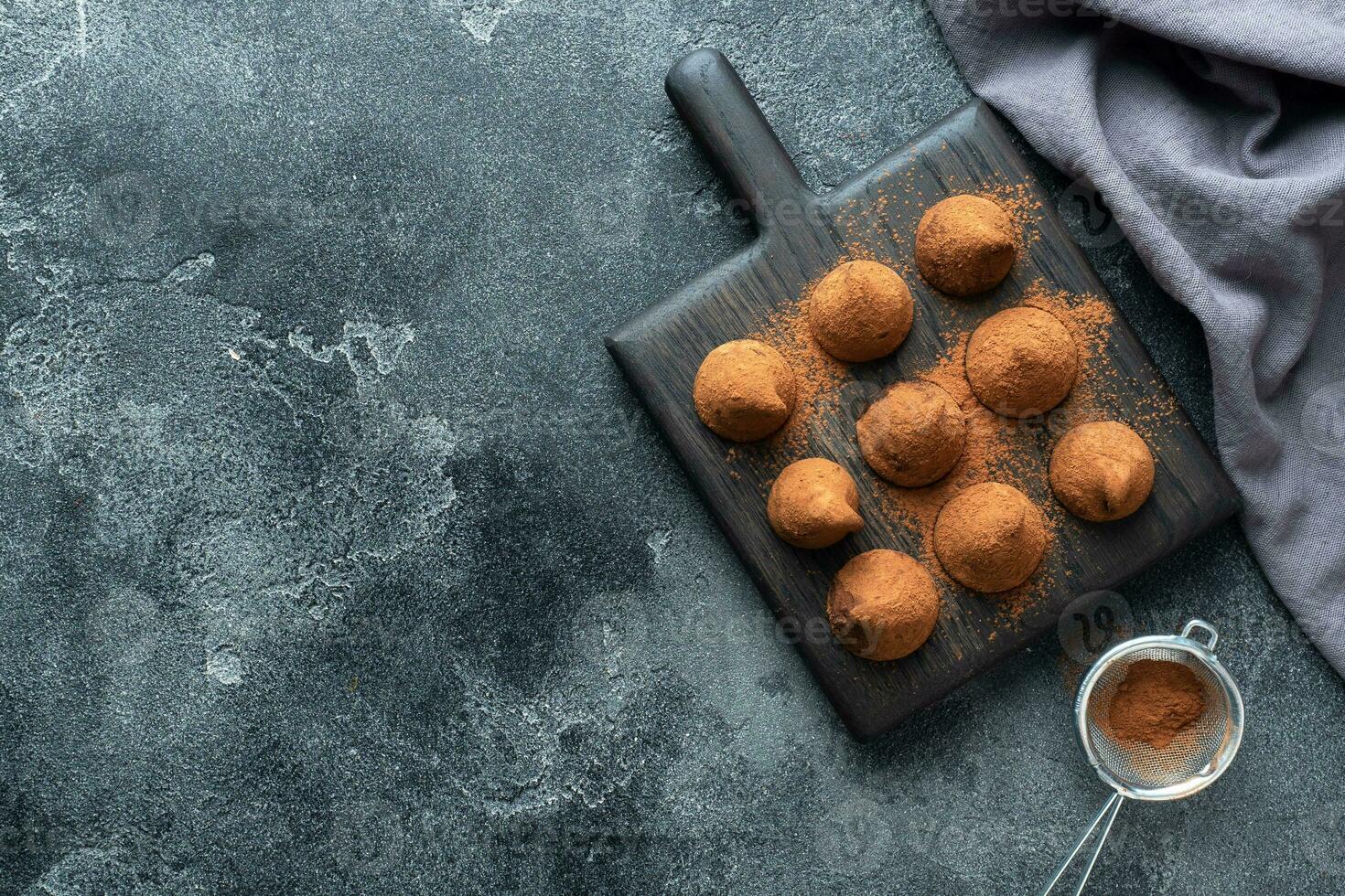 Delicious chocolate truffles sprinkled with cocoa powder and walnuts on a wooden stand. Dark concrete background. Copy space. photo