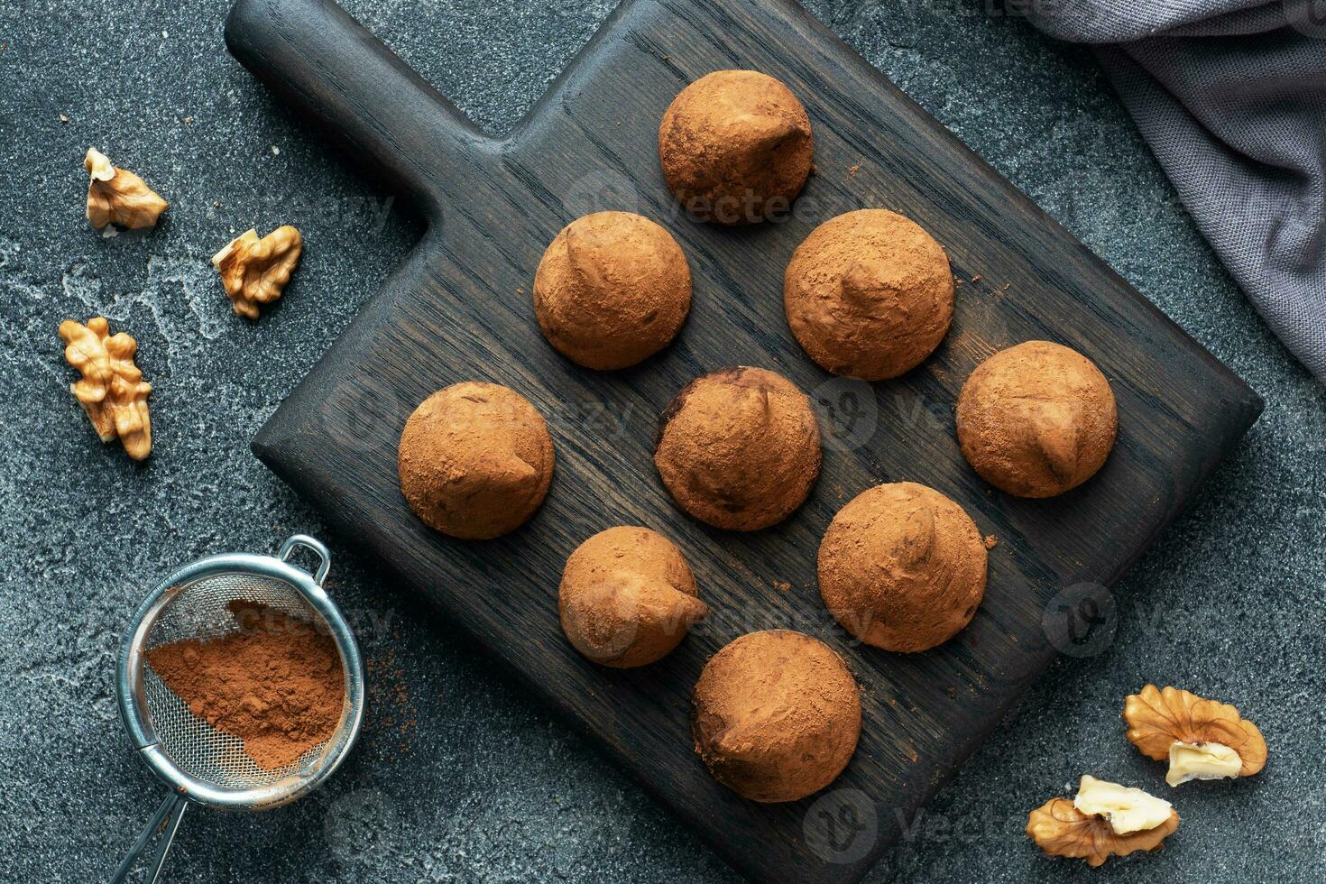 Delicious chocolate truffles sprinkled with cocoa powder and walnuts on a wooden stand. Dark concrete background. photo