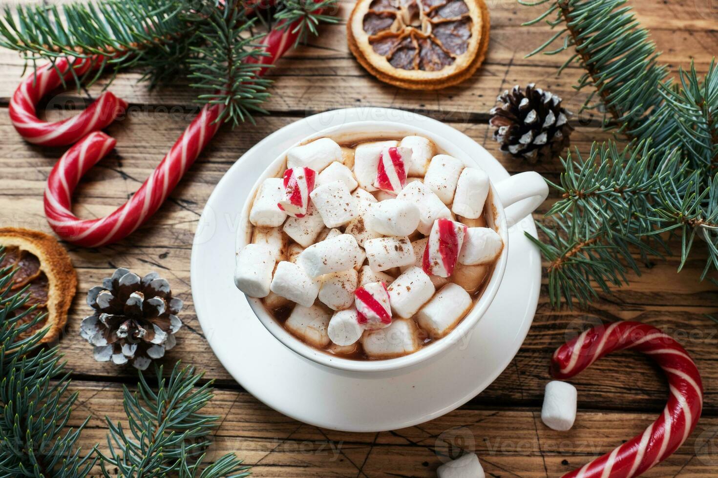 A Cup of hot chocolate with marshmallows. Christmas tree and decorations, cane caramel and oranges nuts Wooden background photo