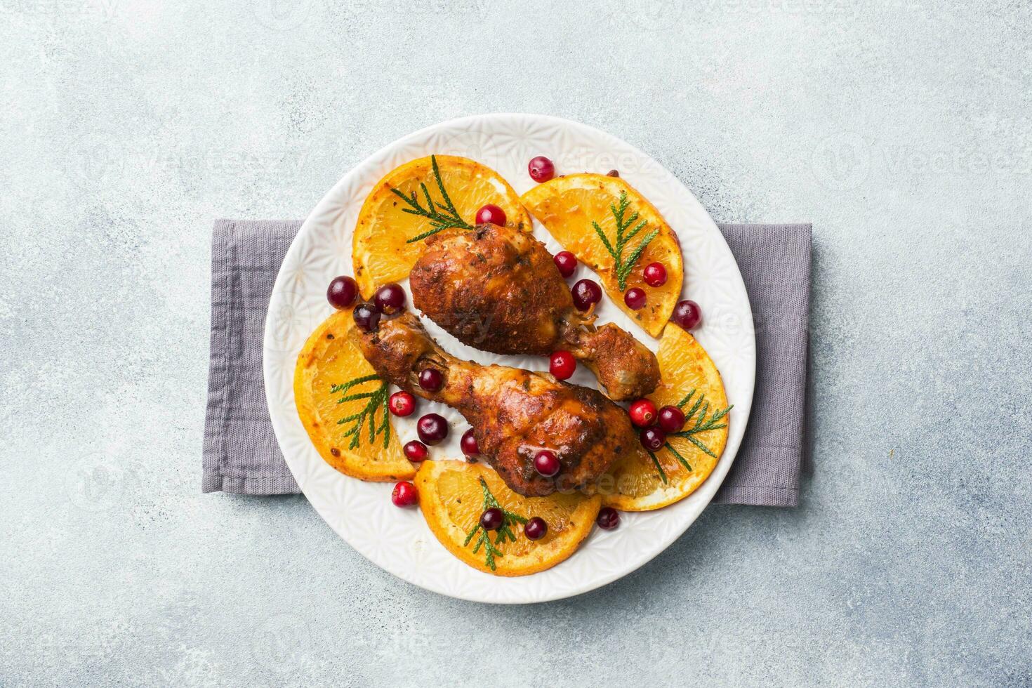 Baked chicken drumstick with oranges and cranberries in a plate light grey background. Christmas food Table with decorations. Copy space. photo