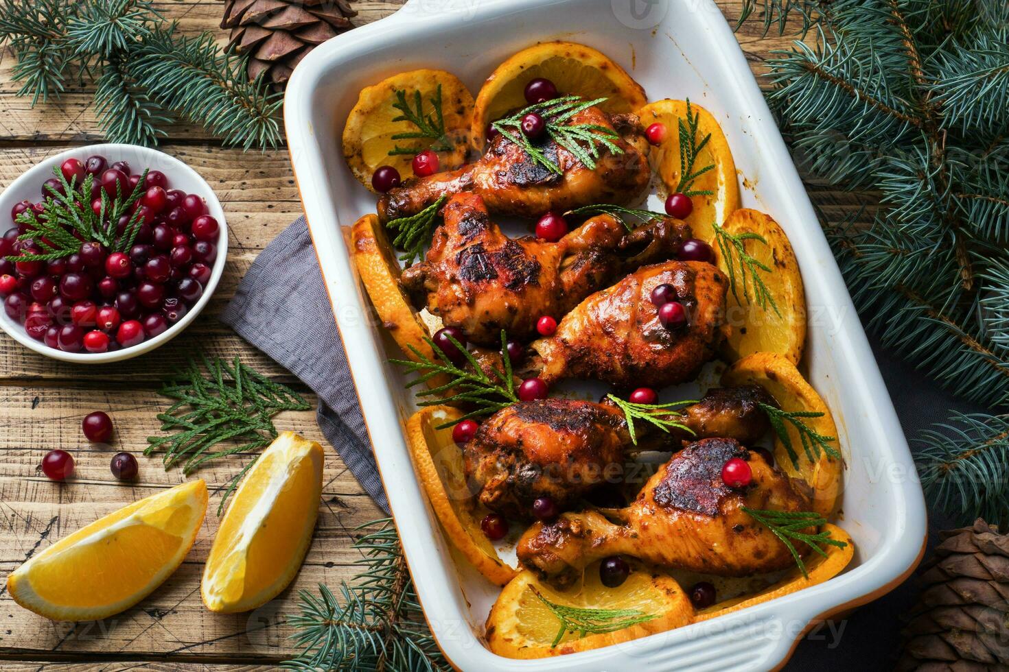 Baked chicken drumstick with oranges and cranberries in a baking sheet on a wooden background. Christmas food Table with decorations. photo