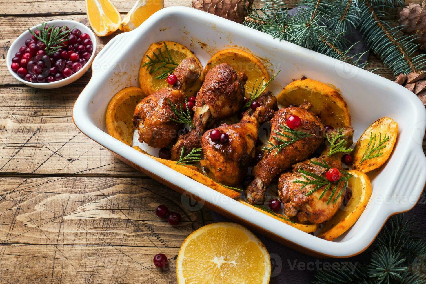 Baked chicken drumstick with oranges and cranberries in a baking sheet on a wooden background. Christmas food Table with decorations. photo