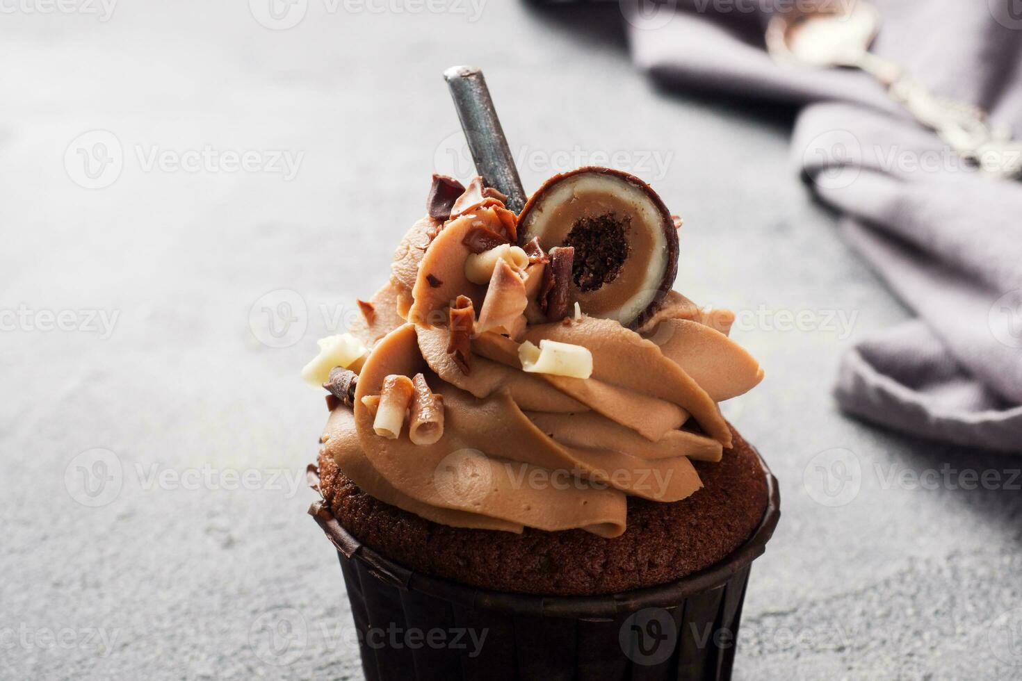 Chocolate muffin with cream decorated with candy and chocolate chips. Dark concrete background. Copy space. photo