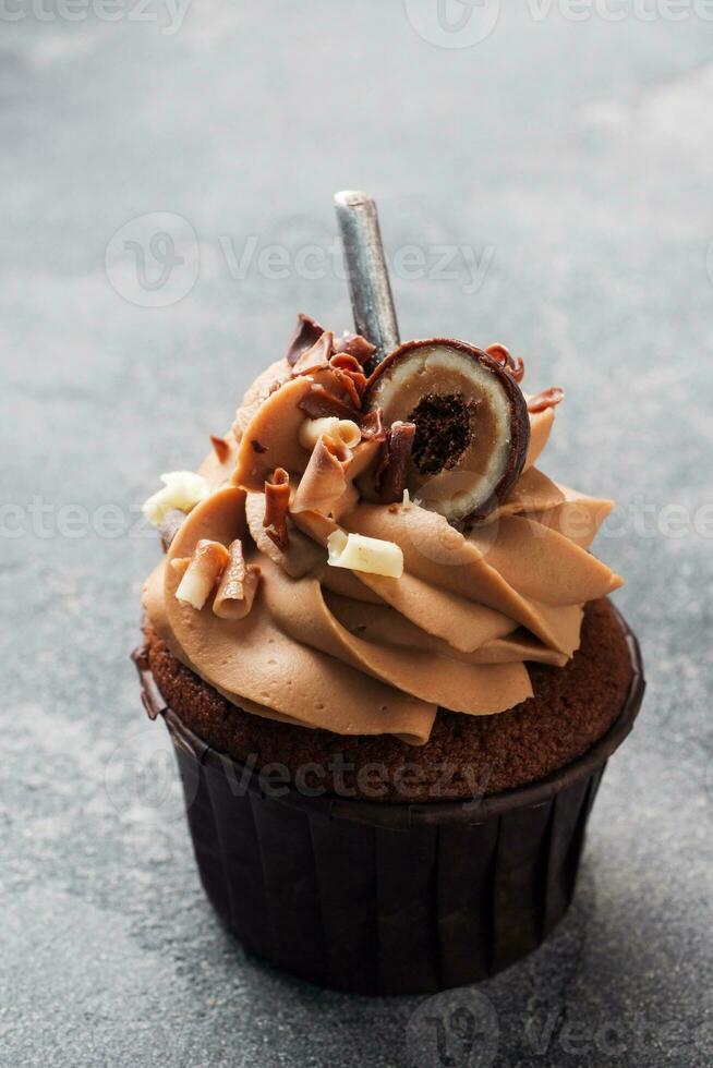 Chocolate muffin with cream decorated with candy and chocolate chips. Dark concrete background. Copy space. photo