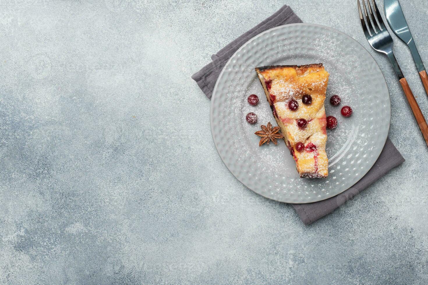 A piece of cottage cheese pie casserole with cranberry berries and spices cinnamon and anise on a plate. Grey concrete background. Copy space. photo