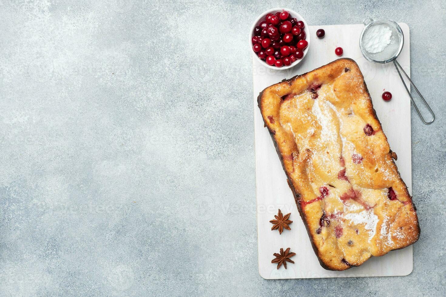 Cottage cheese pie casserole with cranberries and spices sprinkled with powdered sugar on a wooden stand. Gray concrete table. Copy space photo