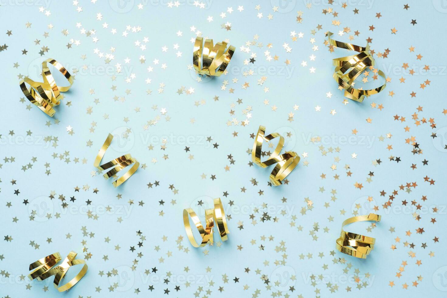 Flat lay background for celebration Christmas and New Year. gold ribbons bows and confetti stars on a blue background. top view copy space. photo