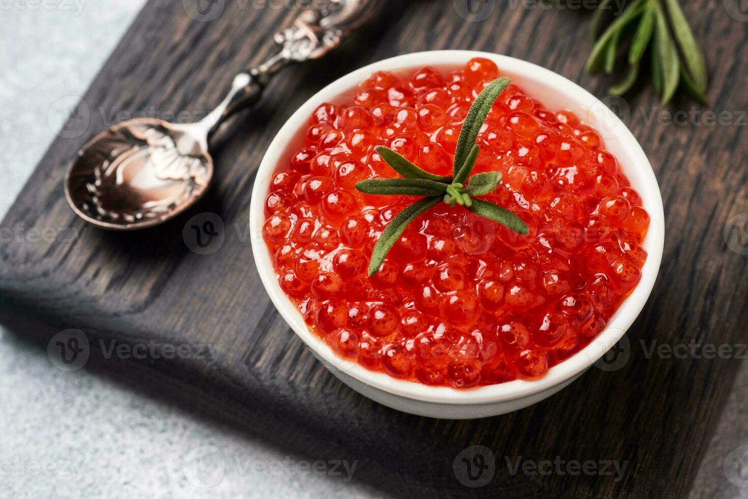 Red salmon caviar in a plate on a wooden cutting Board. Gray concrete background. Snack delicacy. Close up. photo