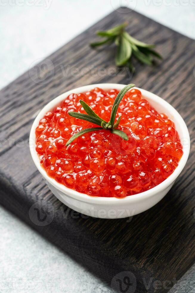 Red salmon caviar in a plate on a wooden cutting Board. Gray concrete background. Snack delicacy. Close up. photo