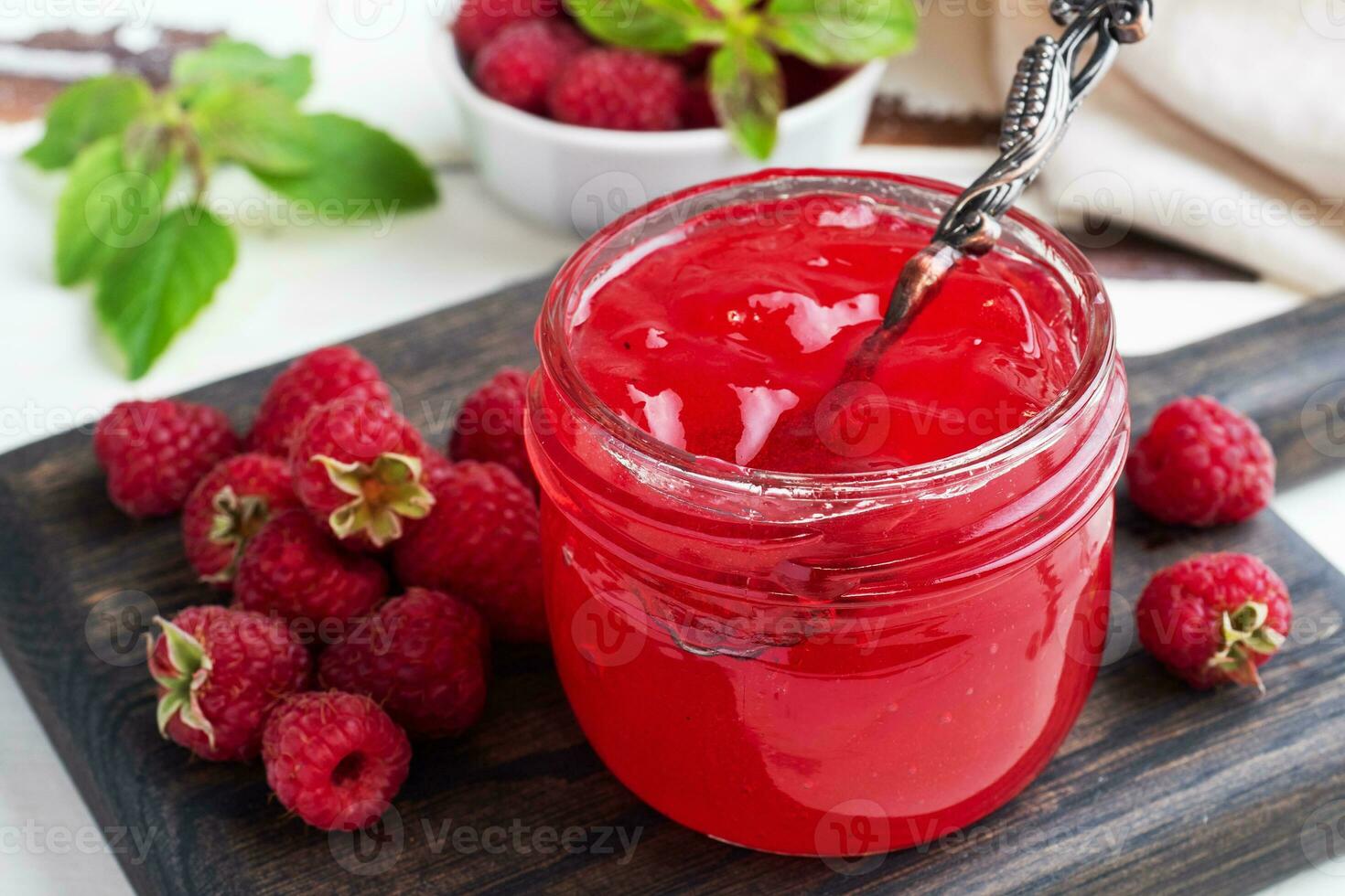 Homemade raspberry jam in a glass jar and fresh raspberries with mint on a wooden rustic background. Close up. photo
