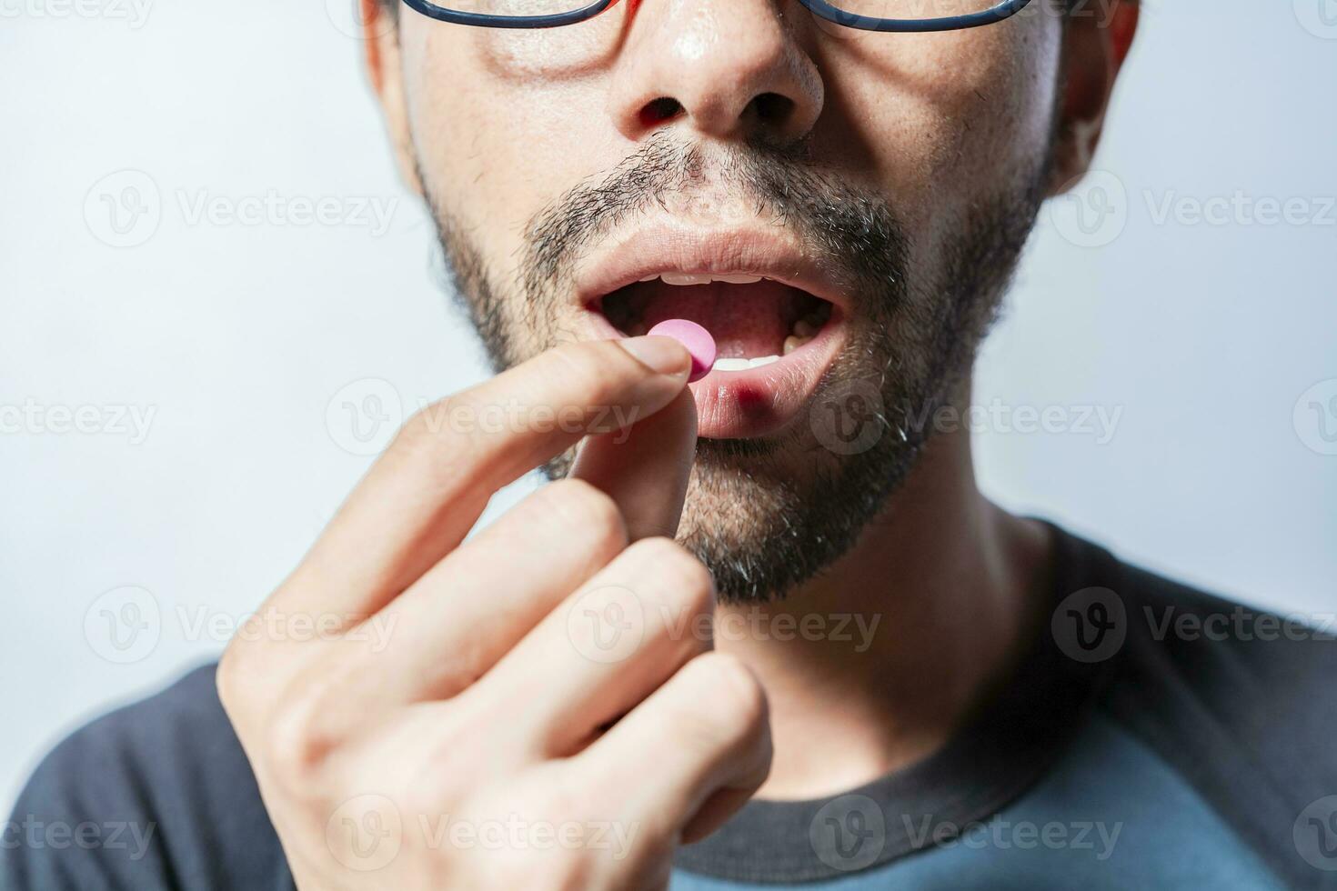Person taking a pill isolated, Close up of young man putting a pill in his mouth. Self-medication concept, Man putting a pill in his mouth isolated, Close-up of a man taking an aspirin photo
