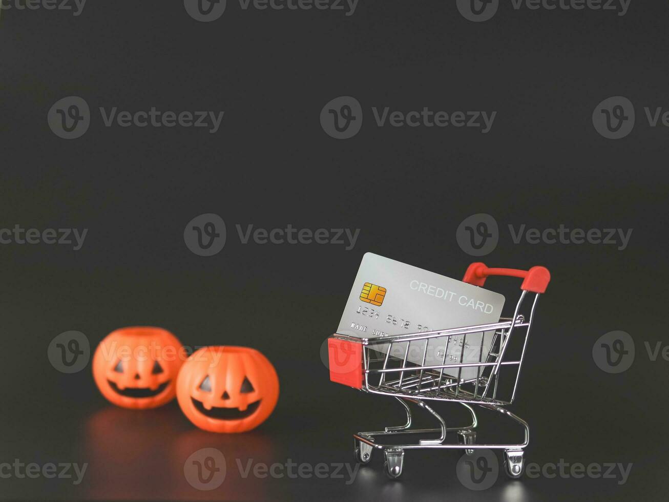 shopping cart or trolley and credit card wiht plastic Halloween pumpkin   isolated  on black  background  holiday shopping  concept. photo