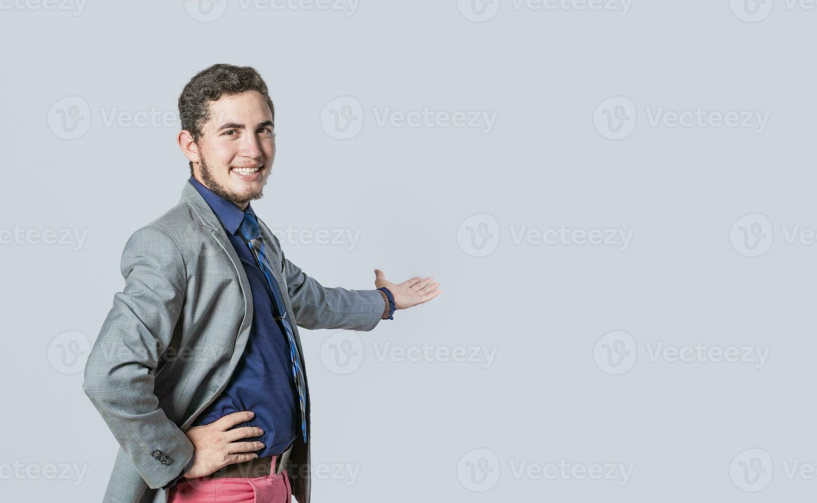 Man pointing back and presenting a product, man in a suit welcoming, man looking at the camera presenting a product, person inviting photo