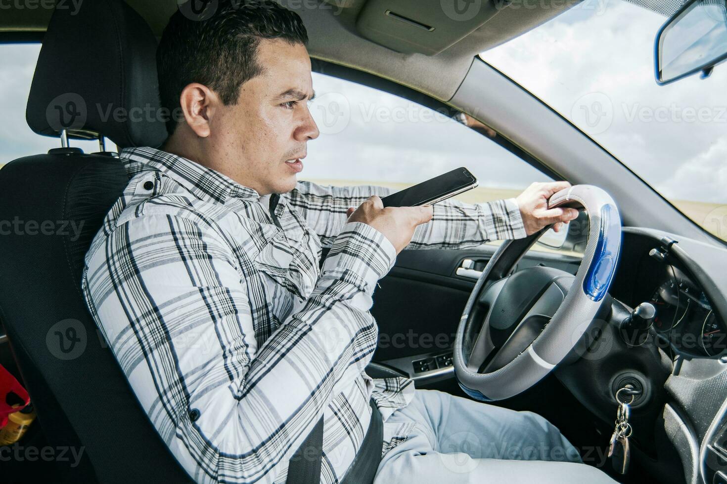 Man in his car sending voice notes with his cell phone, Side view of a young man sitting inside the car talking on the phone while driving photo