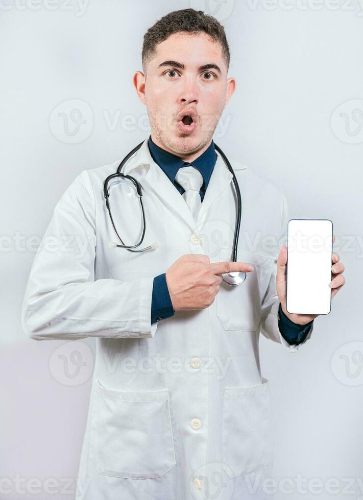 Shocked doctor pointing an application on the cell phone. Amazed young doctor holding and pointing cell phone screen photo