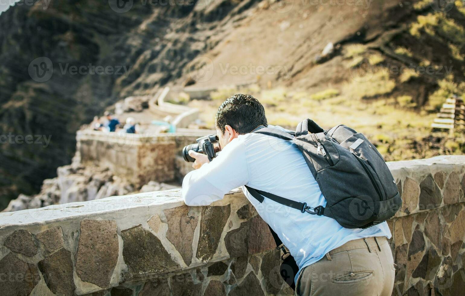 A tourist man with a photo camera taking photos at a viewpoint. Adventurous man with his camera taking photos at a viewpoint. Close up of tourist man taking photos at a volcanic viewpoint