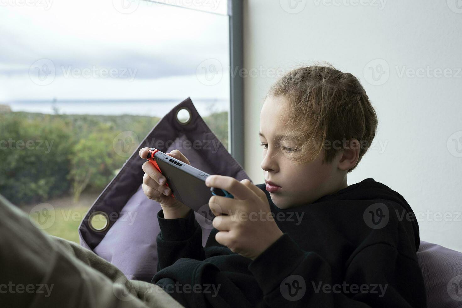 Boy teenager being attracted with game on handheld console photo