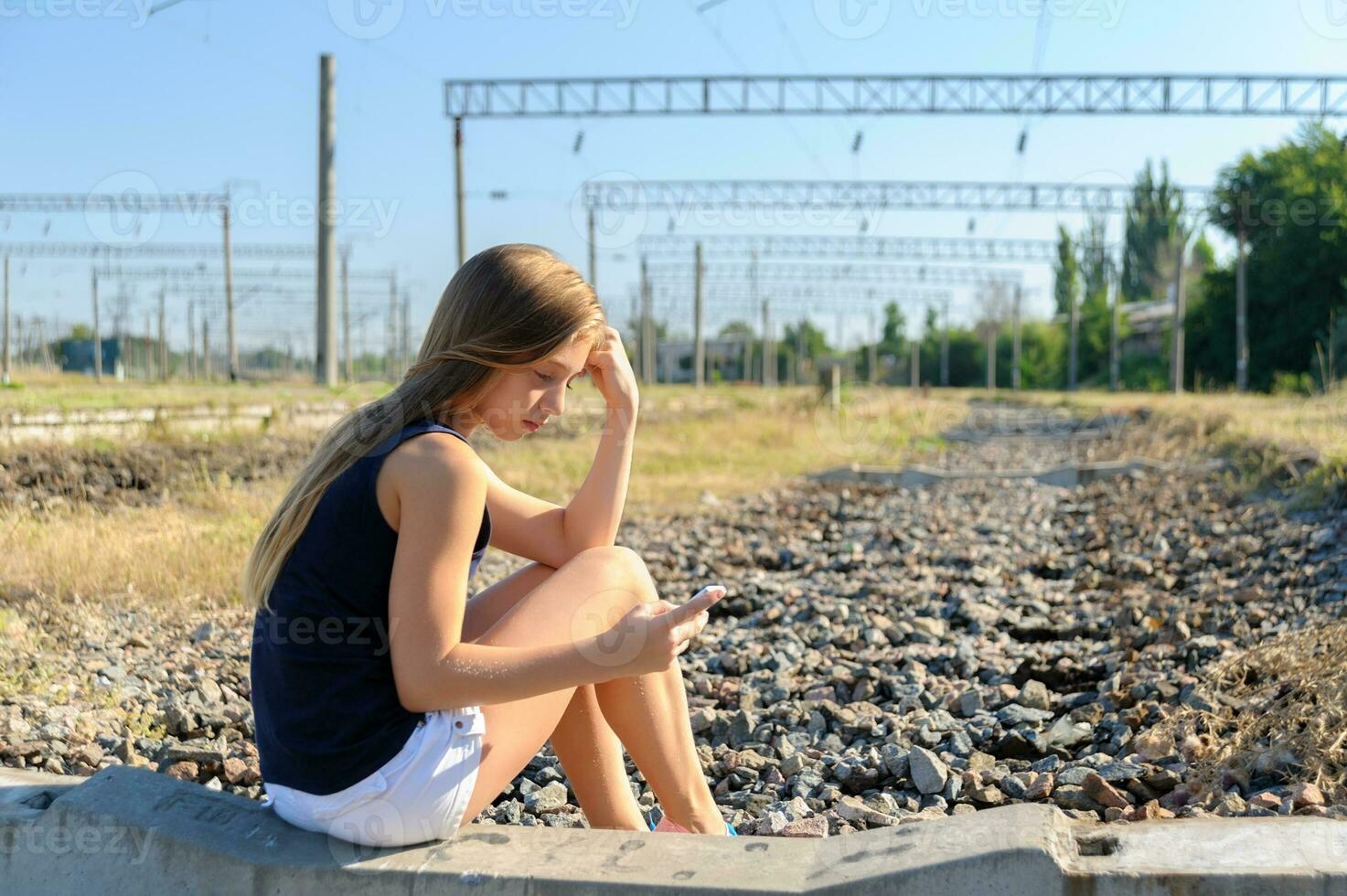 Teenager girl with mobile sitting on unfinished rail track photo