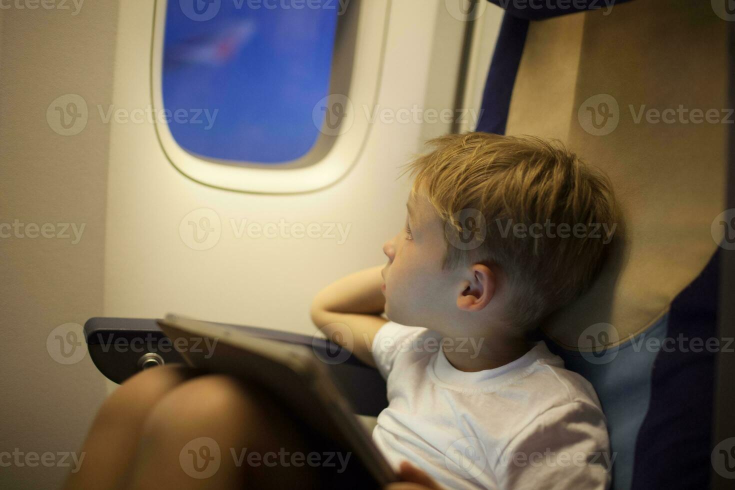 Boy in plane looking out illuminator with pad on lap photo