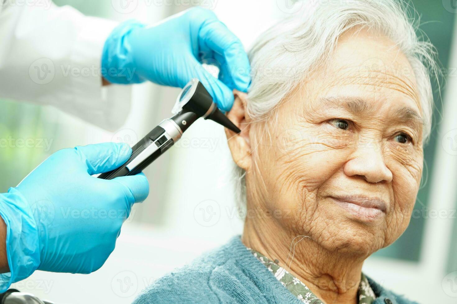 Otolaryngologist or ENT physician doctor examining senior patient ear with otoscope, hearing loss problem. photo