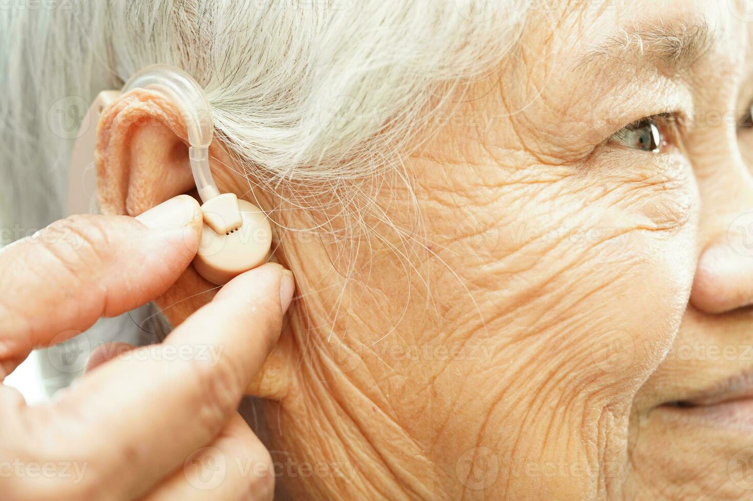 Doctor install hearing aid on senior patient ear to reduce hearing loss problem. photo