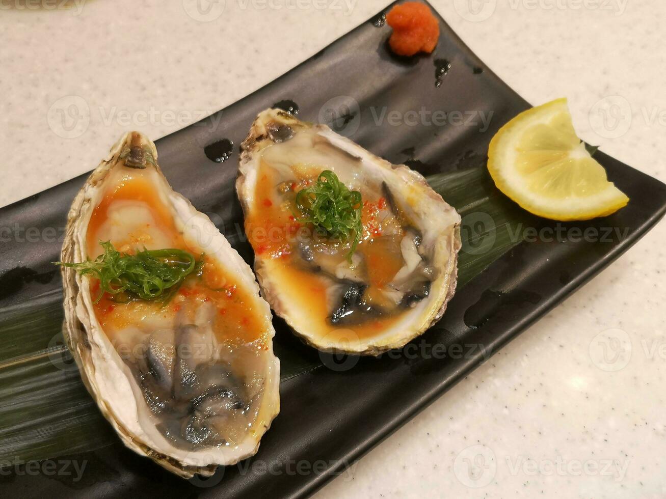 Spicy oysters with lemon in a black plate on a table background. photo