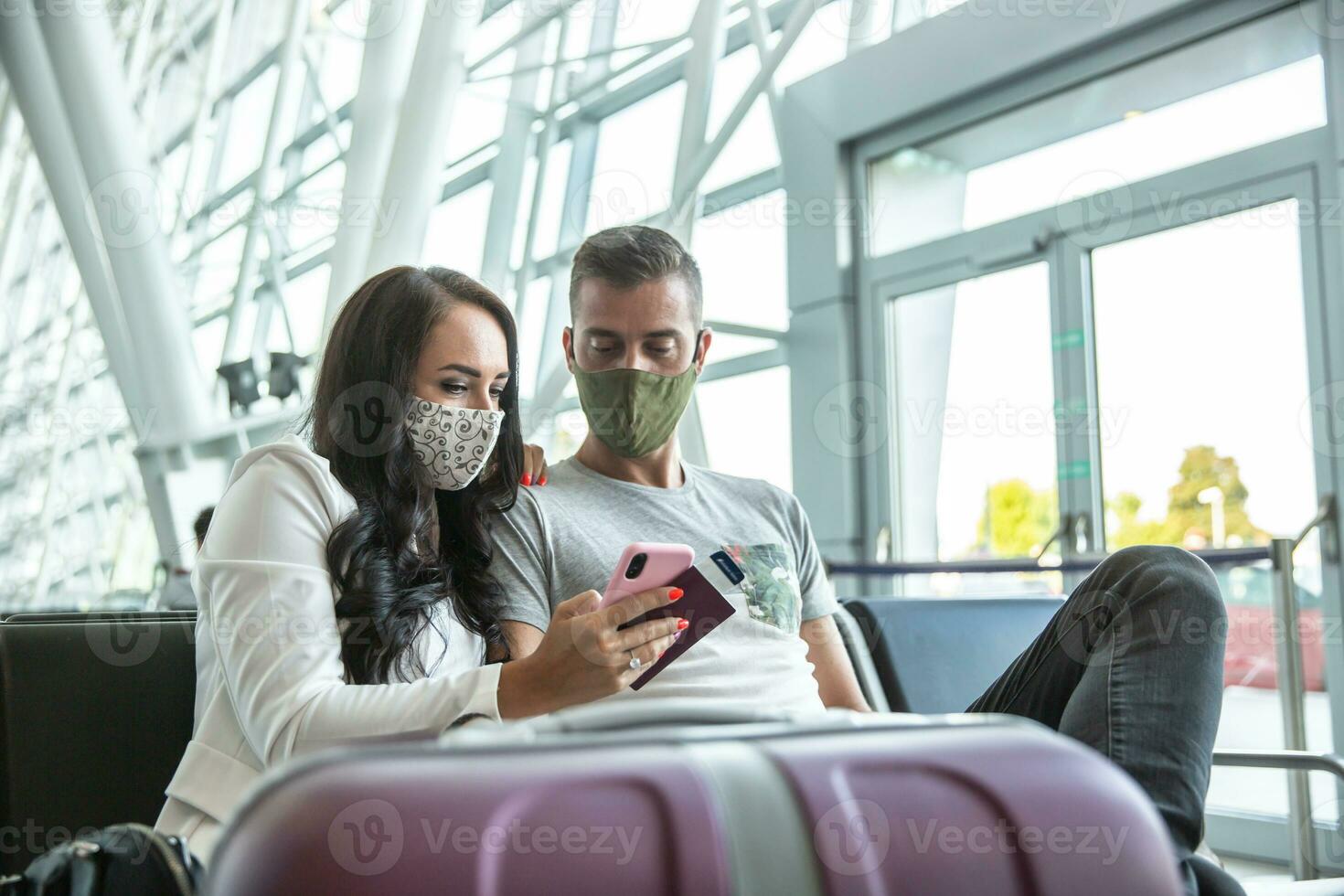 Travelling couple in face masks check latest updated on a mobile phone during waiting in an airport terminal photo