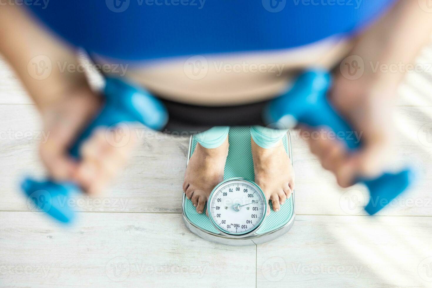 Heavy fat woman stands on a scale and holds dumbbells in her hands photo