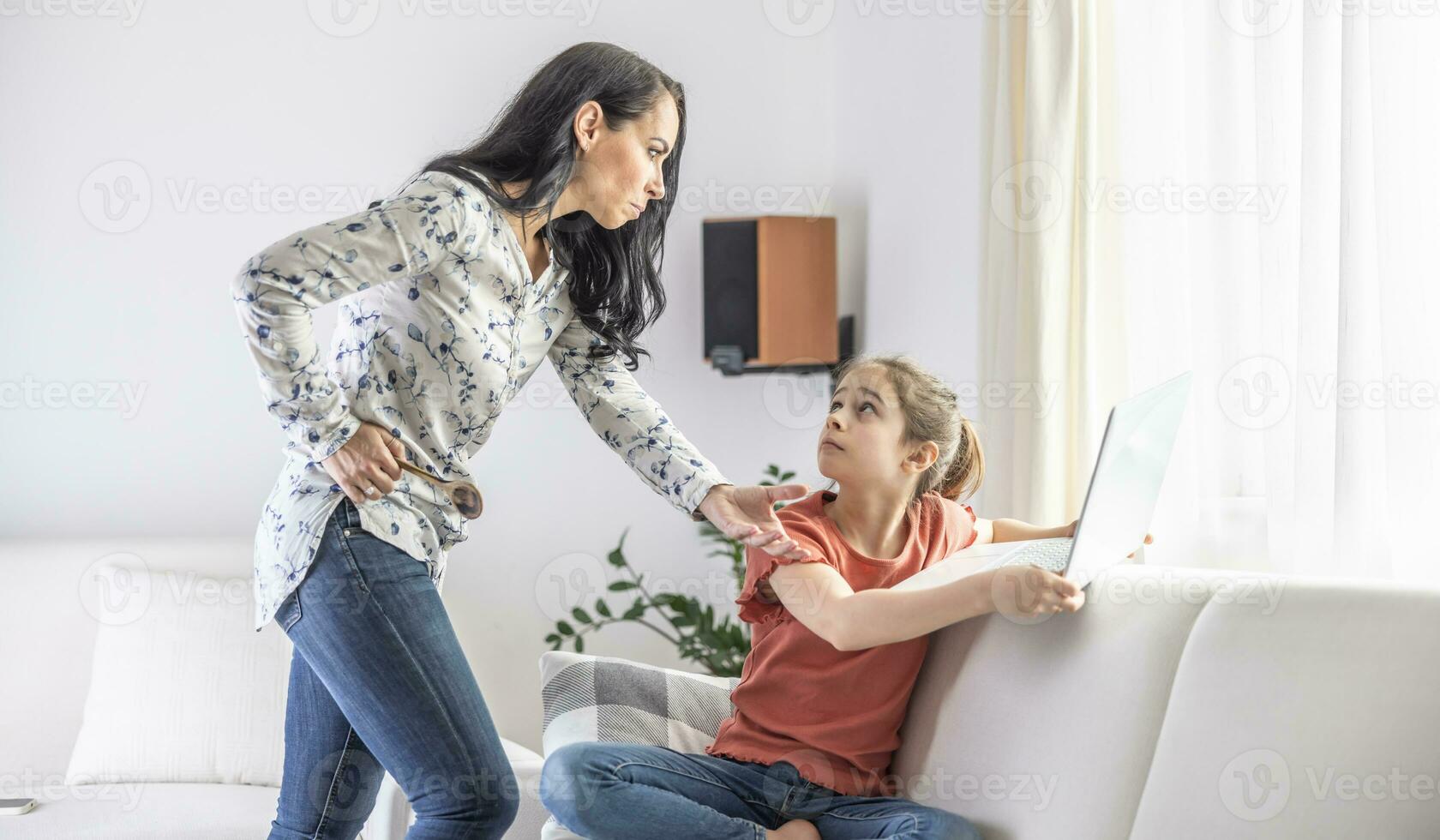 Abusive woman reaches to take the laptop away from a young girl who looks fearfully at her photo