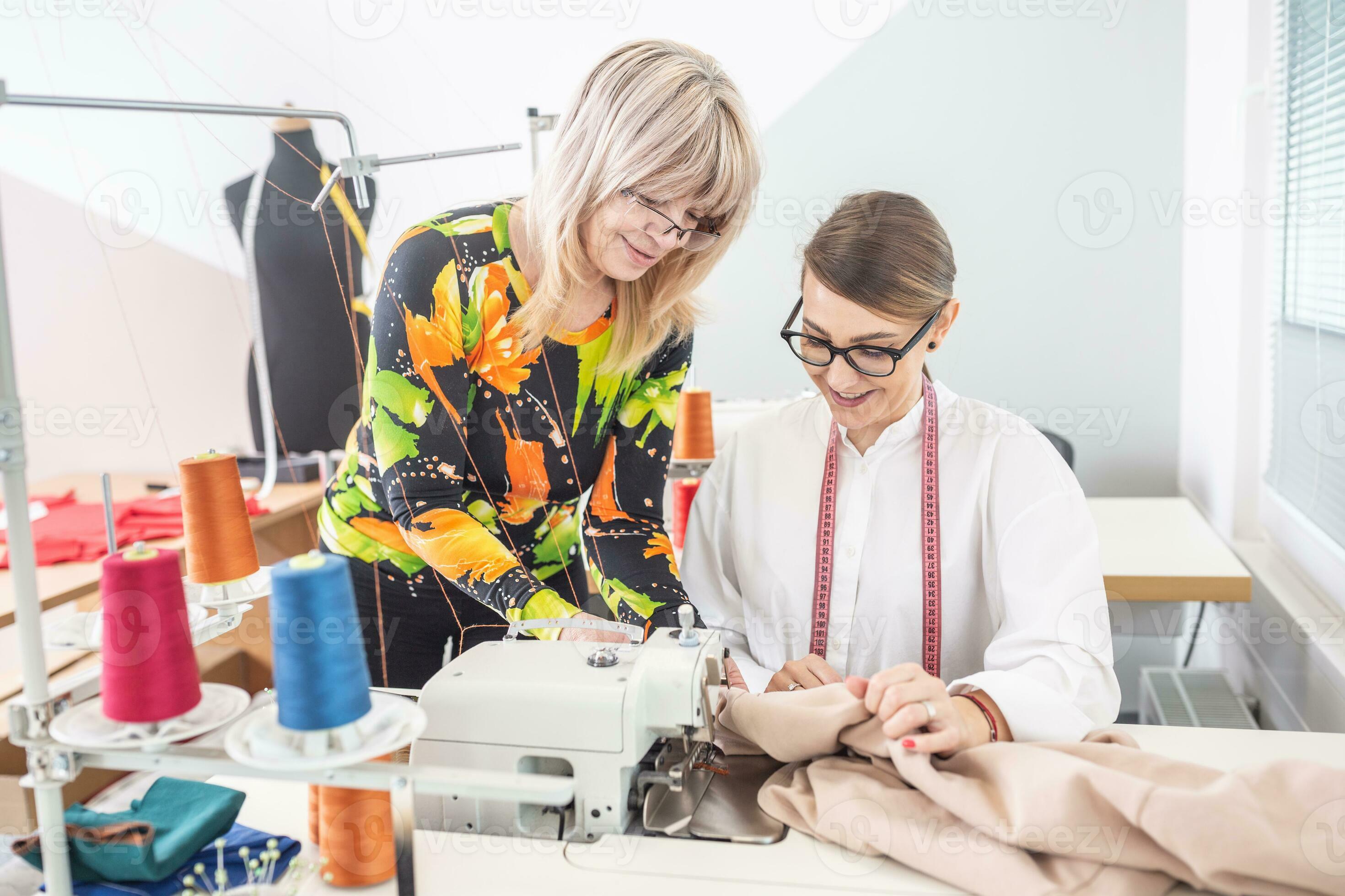 Experiences female tailor shows details of work on clothing to a yound apprentice sitting behind
