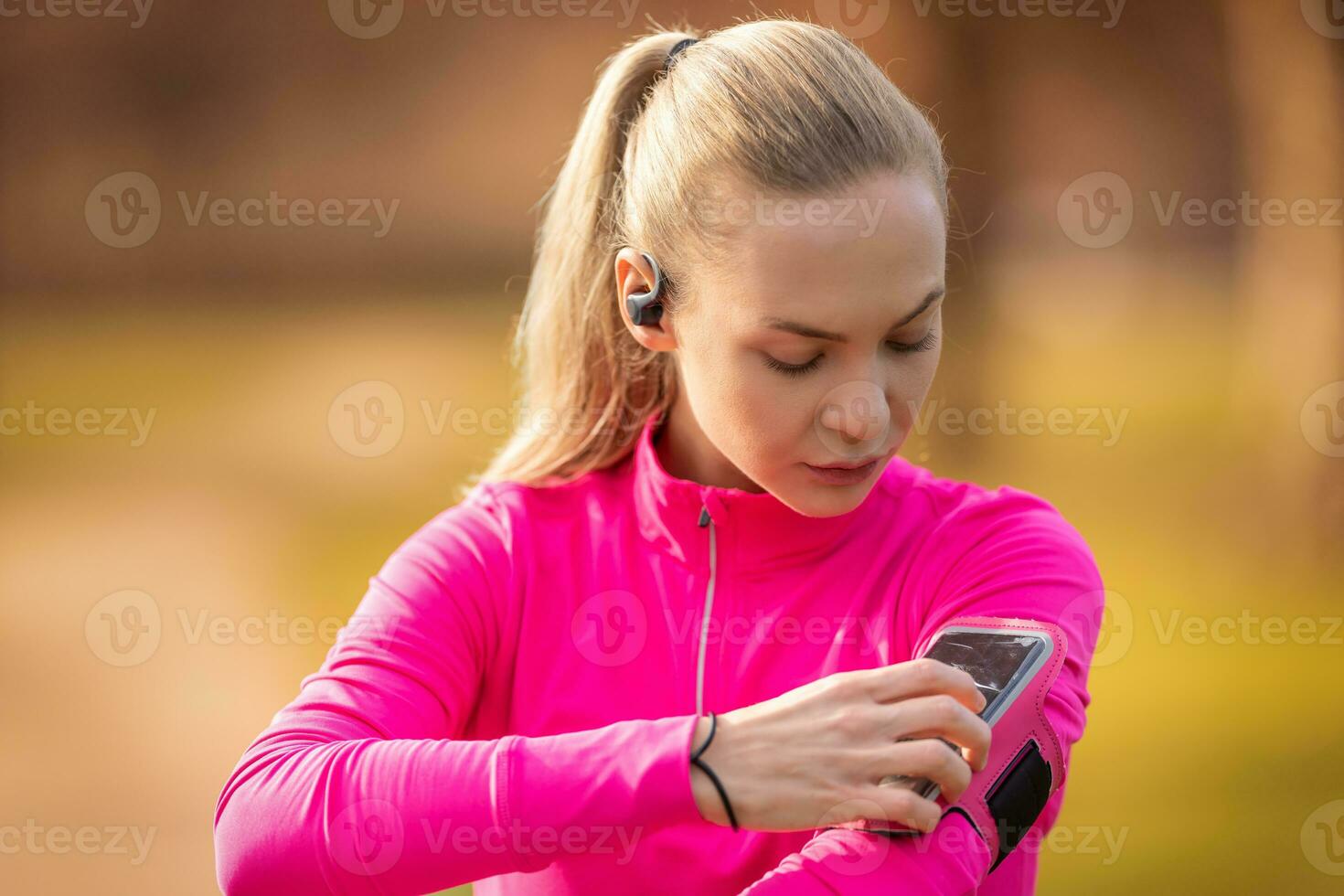 A beautiful young athlete with a mobile phone on her shoulder starts running by launching a sports app photo