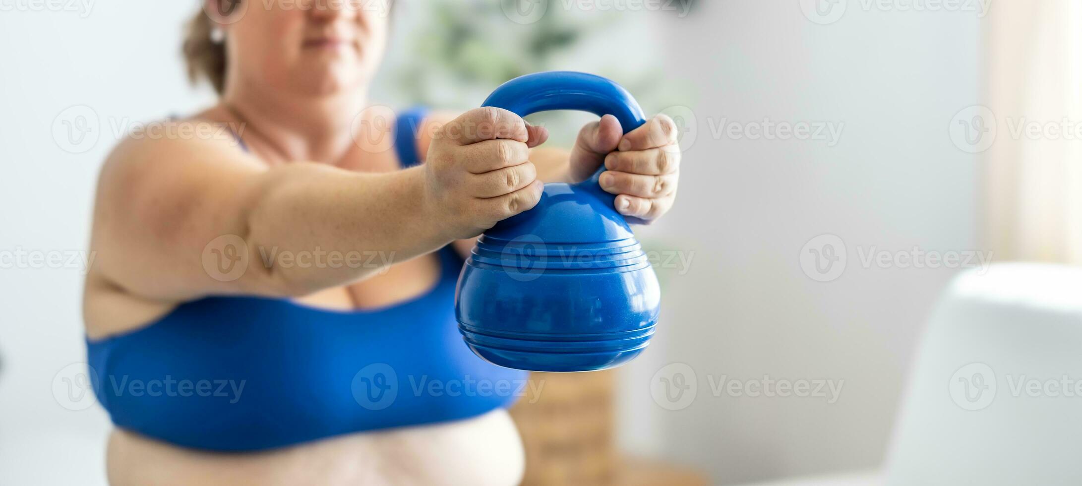 Plus size woman doing exercises with dumbbells, strengthening her body in living room, selective focus photo