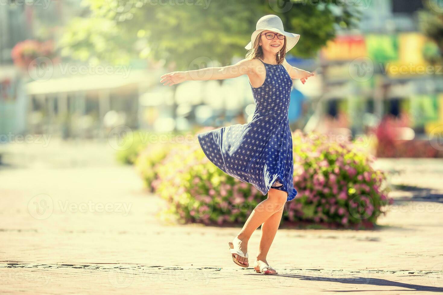 Beautiful cute young girl dancing on the street from happiness.Cute happy girl in summer clothes dancing in the sun. photo