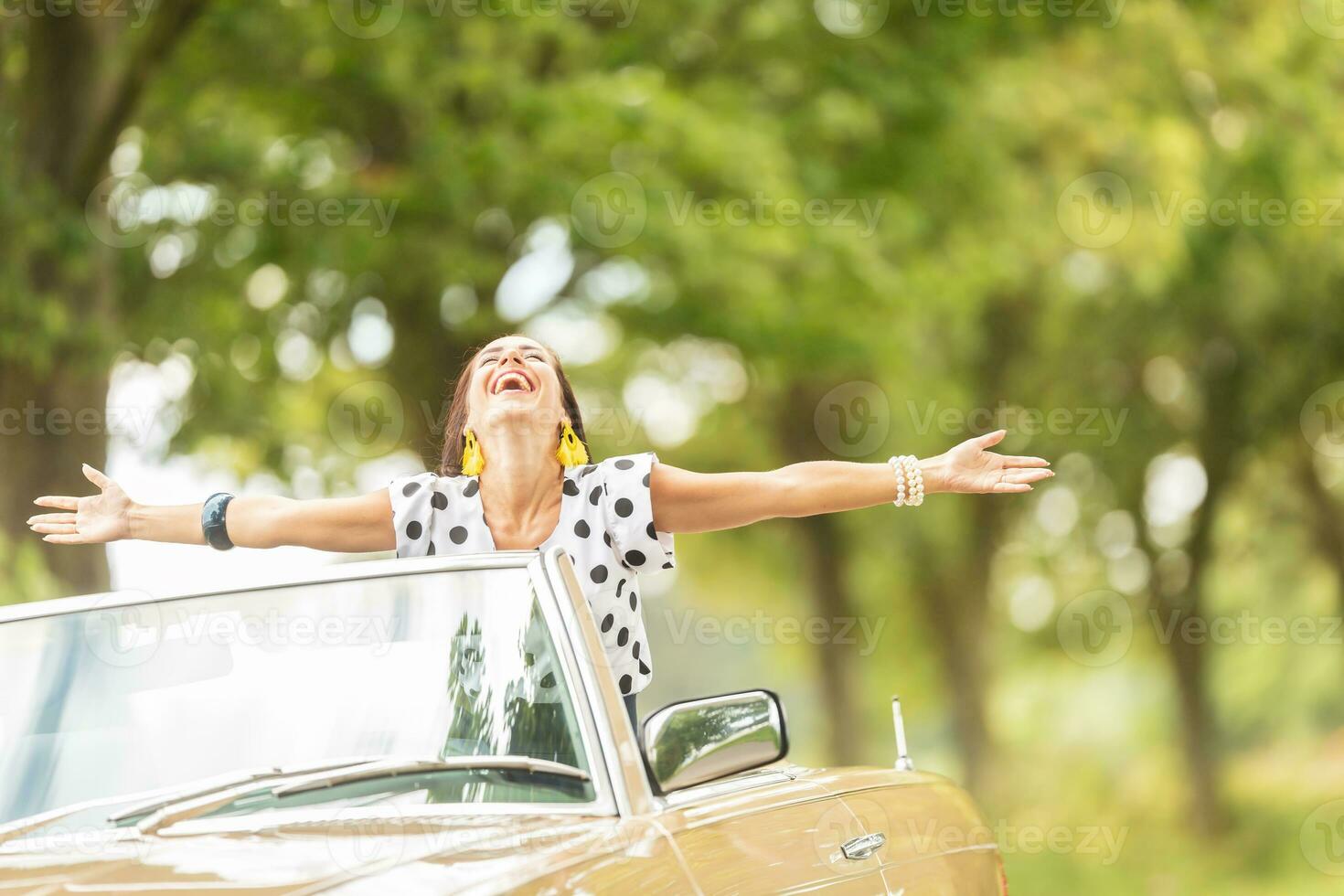 contento mujer con brazos amplio abierto disfrutando libertad en un convertible automóvil viaje foto