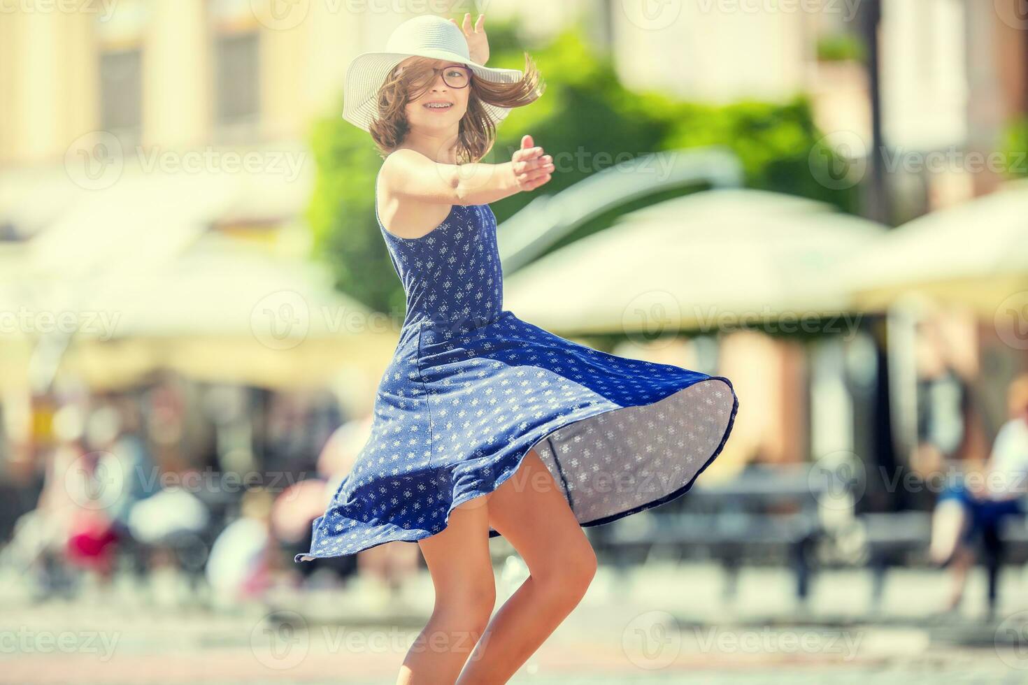 Beautiful cute young girl dancing on the street from happiness.Cute happy girl in summer clothes dancing in the sun. photo