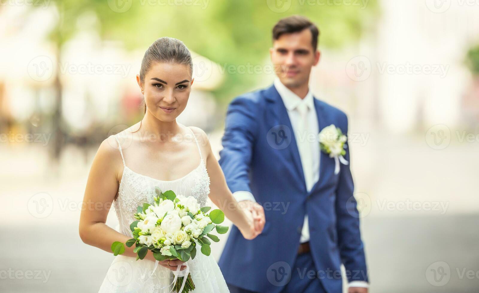 Charming couple holding eeach others hand while wanking in the town. They are wearing wedding robes and holding nice flowers photo