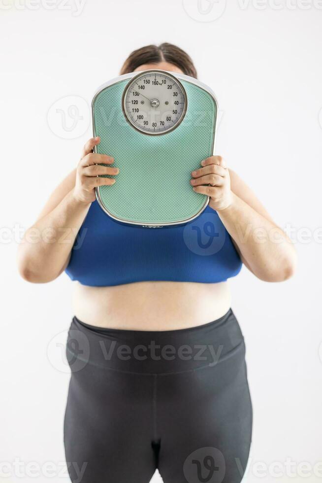 A very overweight woman holds a scale showing her weight in front of her head photo