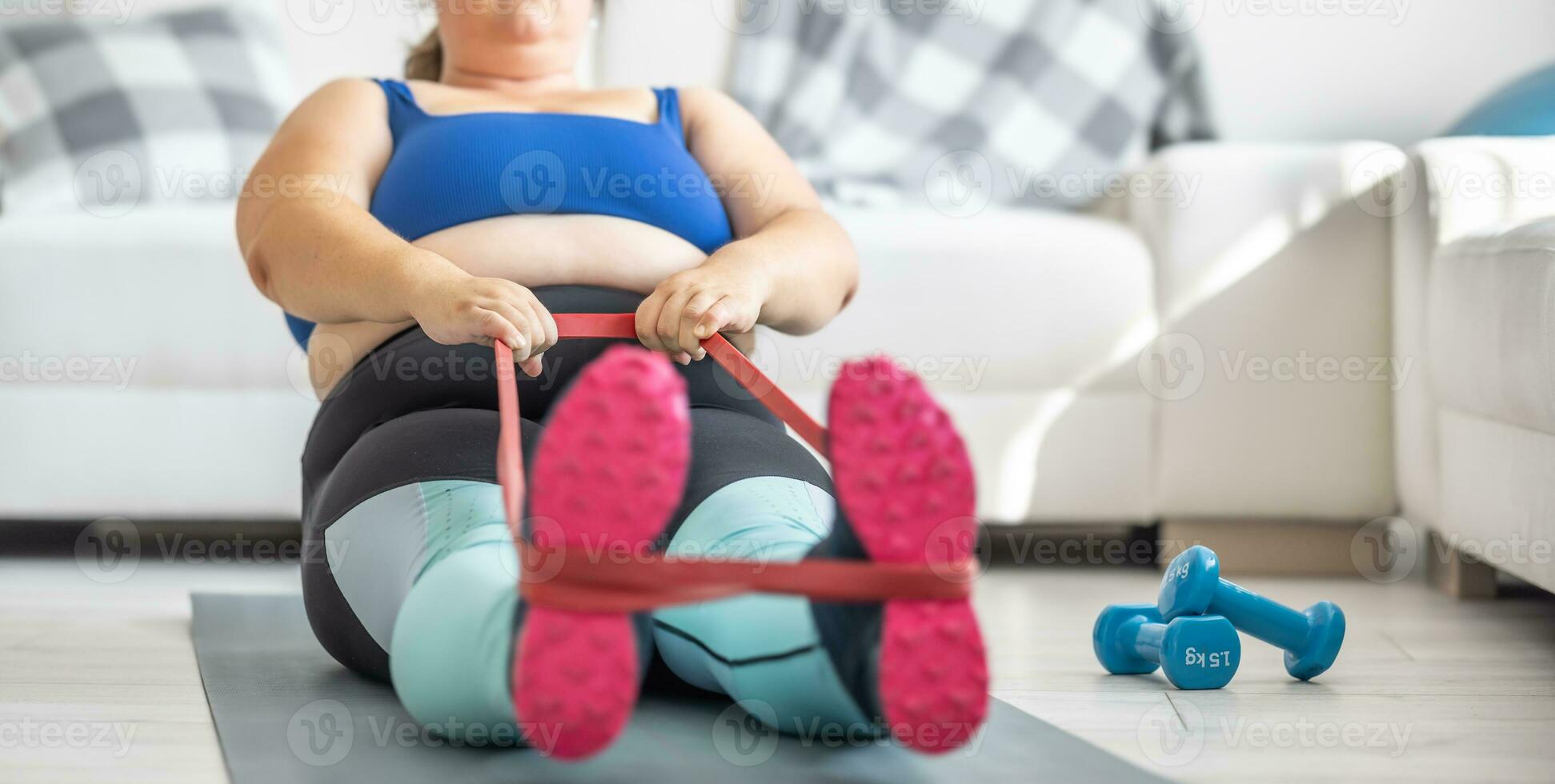 Overweight lady doing sports exercise in living room. He lies on the mat and stretches the sports rubbers photo