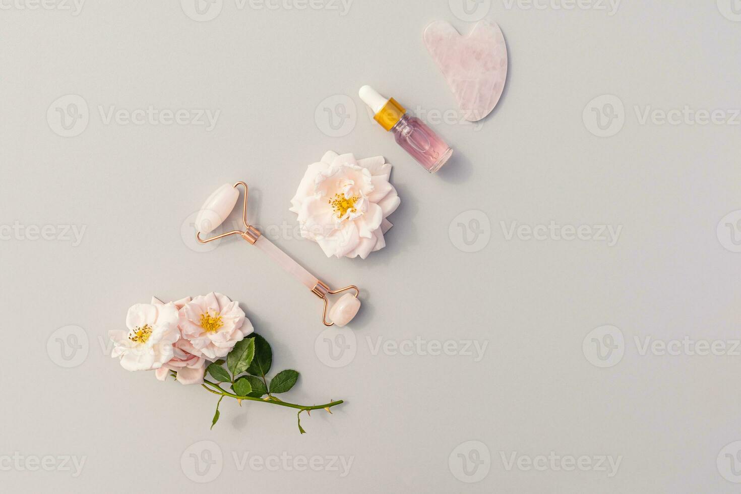 quartz roller, gua sha scraper,cosmetic bottle with rose oil or serum for face and neck skin care and massage. Top view. Flat layout photo