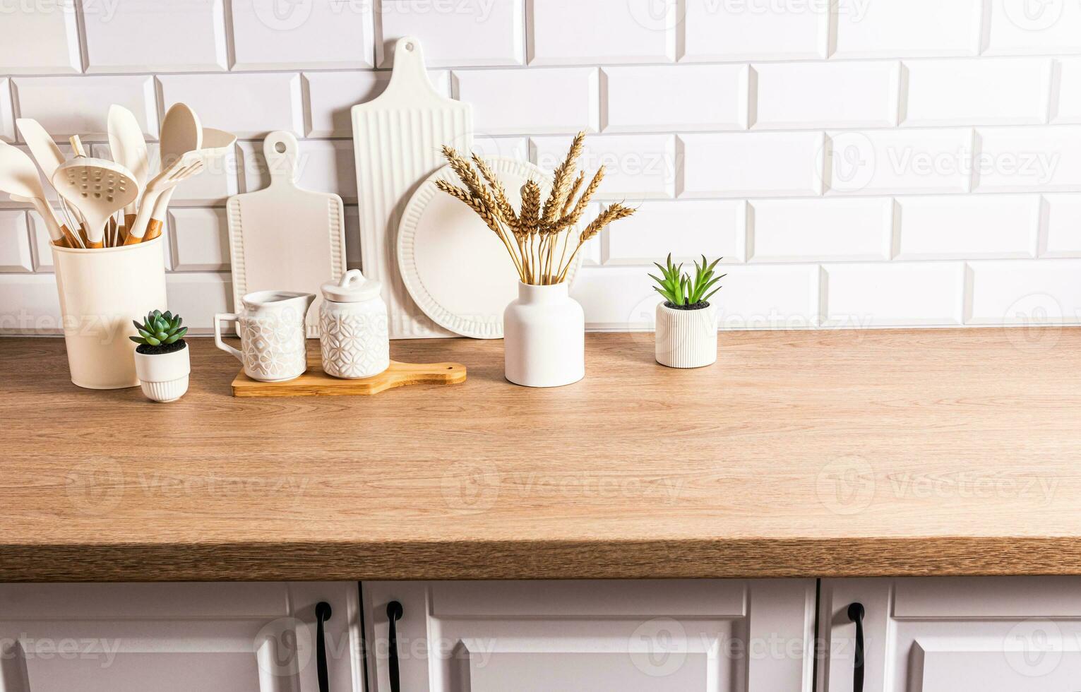 White ceramic utensils and kitchen utensils on a wooden countertop in an eco-friendly kitchen with green indoor plants. Cozy house photo