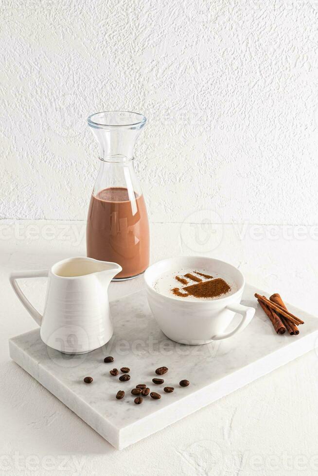 un grande blanco taza de delicioso aromático capuchino café en un blanco mármol bandeja con canela palos y café frijoles. vertical vista. foto
