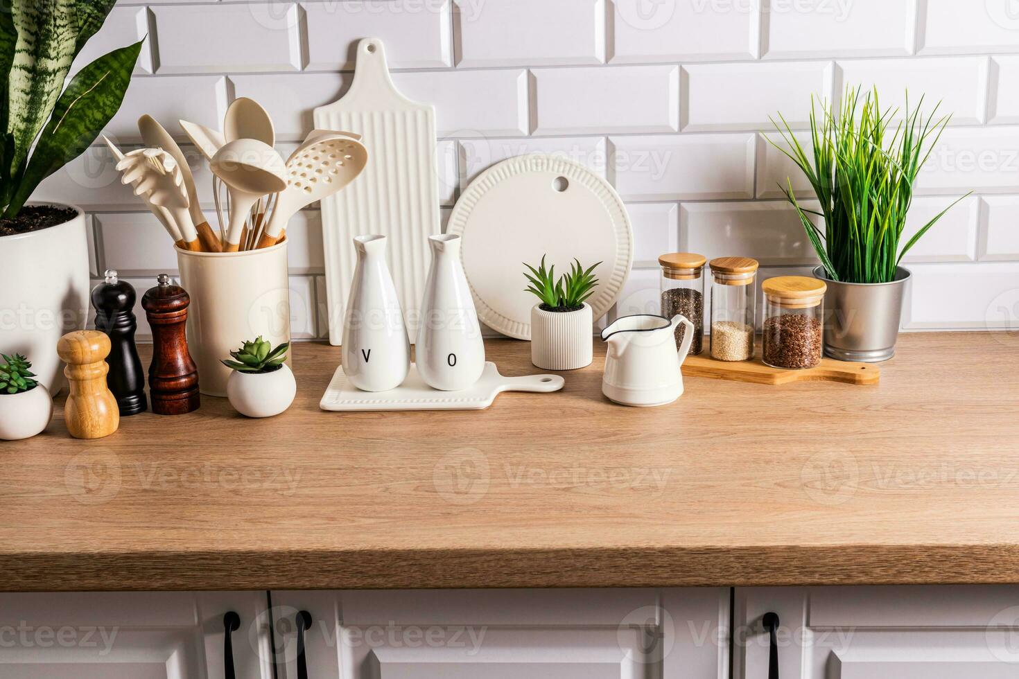White ceramic utensils and kitchen utensils on a wooden countertop in an eco-friendly kitchen with green indoor plants. Cozy house photo