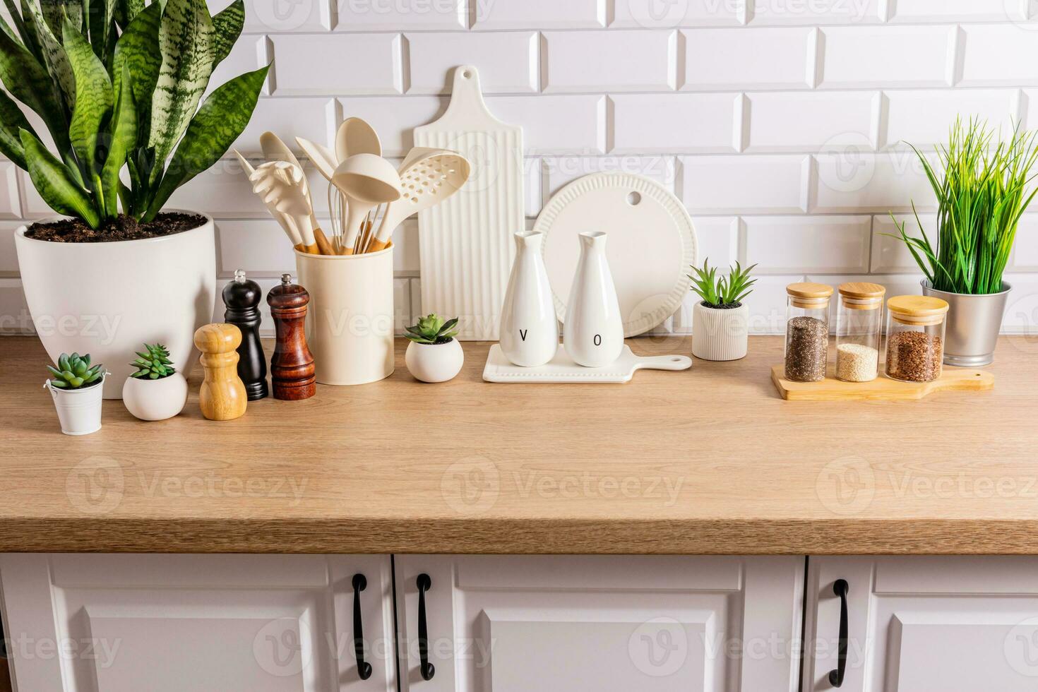 White ceramic utensils and kitchen utensils on a wooden countertop in an eco-friendly kitchen with green indoor plants. Cozy house photo